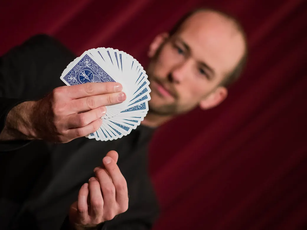 Zauberkünstler Andreas Maier fächert ein Kartenspiel vor rotem Bühnenvorhang auf